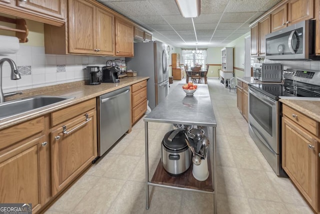 kitchen featuring sink, a paneled ceiling, appliances with stainless steel finishes, an inviting chandelier, and decorative backsplash