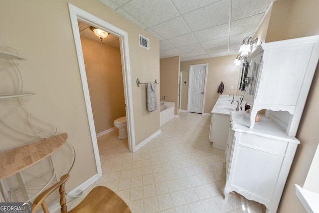 bathroom with vanity, toilet, a drop ceiling, and a tub to relax in