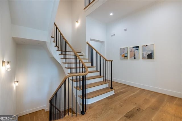 staircase with a towering ceiling and hardwood / wood-style flooring