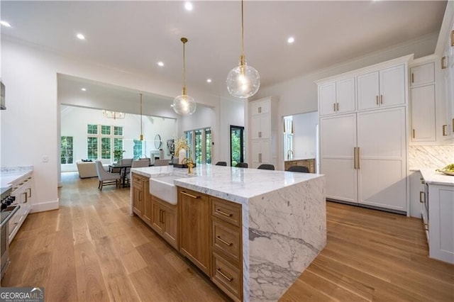 kitchen with light stone countertops, a spacious island, white cabinets, decorative light fixtures, and backsplash