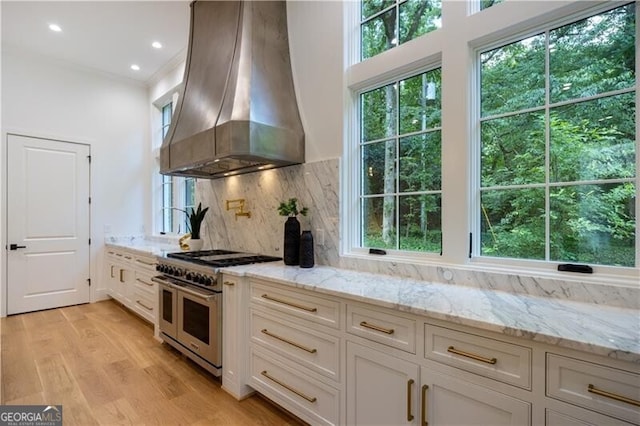 kitchen featuring double oven range, white cabinetry, island range hood, and decorative backsplash