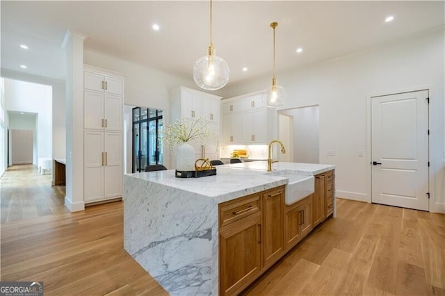 kitchen featuring a large island, light stone counters, sink, white cabinetry, and decorative light fixtures