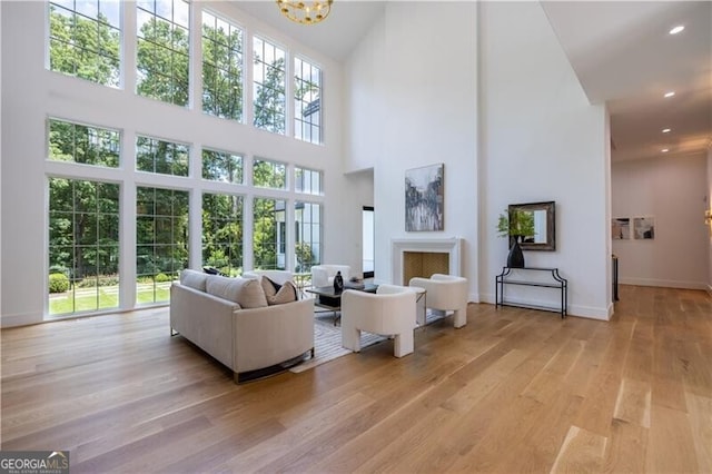 living room featuring a high ceiling, an inviting chandelier, a wealth of natural light, and light hardwood / wood-style flooring