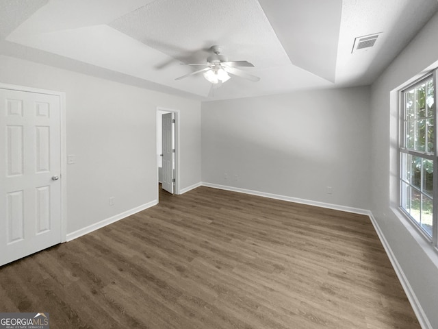 unfurnished room featuring ceiling fan, dark wood-type flooring, a textured ceiling, and a tray ceiling