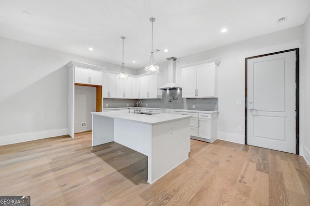 kitchen featuring white cabinets, sink, an island with sink, and wall chimney exhaust hood