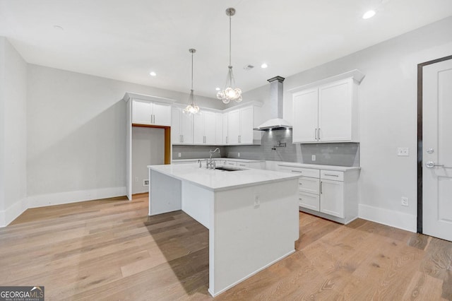 kitchen featuring white cabinets, sink, a center island with sink, and wall chimney range hood