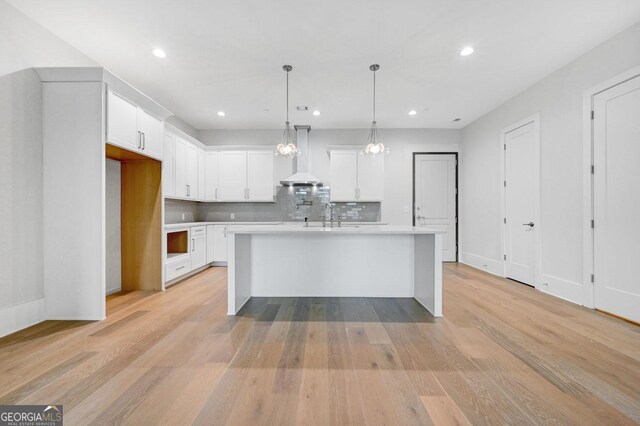 kitchen with white cabinetry, light hardwood / wood-style floors, a kitchen island with sink, and wall chimney range hood