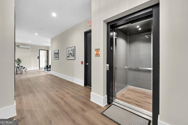 hall featuring elevator, light hardwood / wood-style flooring, and an AC wall unit