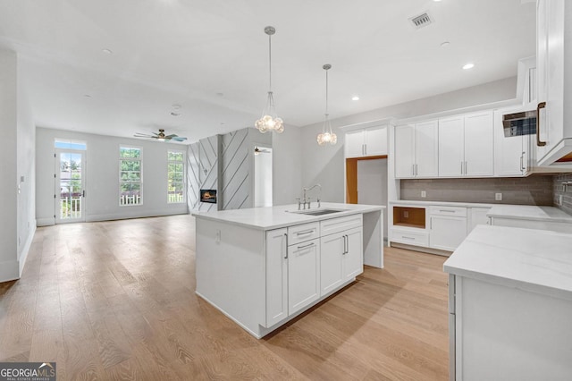 kitchen with hanging light fixtures, a kitchen island with sink, sink, and white cabinets