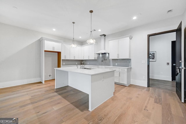 kitchen featuring white cabinetry, an island with sink, hanging light fixtures, and wall chimney range hood