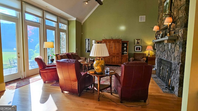 living room with crown molding, high vaulted ceiling, light hardwood / wood-style flooring, and a stone fireplace