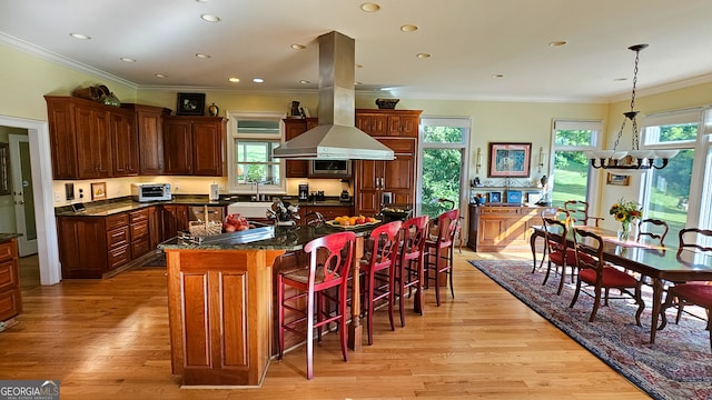 kitchen with island exhaust hood, light hardwood / wood-style flooring, ornamental molding, a center island, and an inviting chandelier