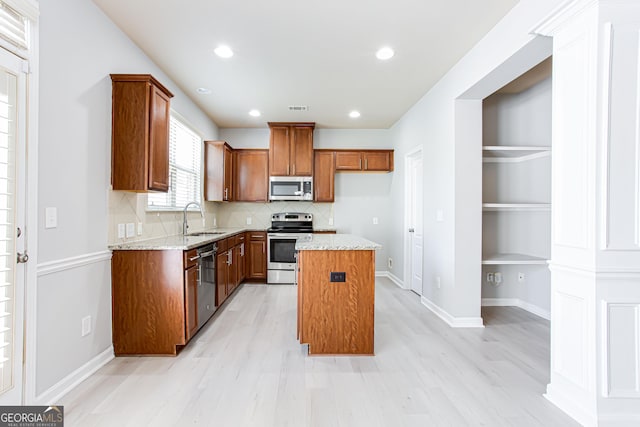 kitchen with stainless steel appliances, backsplash, light wood-type flooring, light stone counters, and a center island