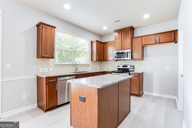 kitchen with light hardwood / wood-style floors, appliances with stainless steel finishes, a kitchen island, light stone counters, and sink