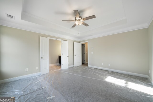 unfurnished bedroom featuring a raised ceiling, carpet, ornamental molding, and ceiling fan