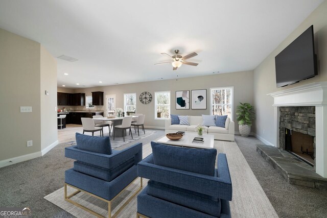 carpeted living room with a stone fireplace and ceiling fan