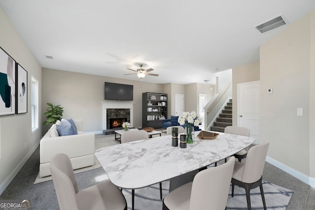 carpeted dining room featuring a wealth of natural light, a stone fireplace, and ceiling fan