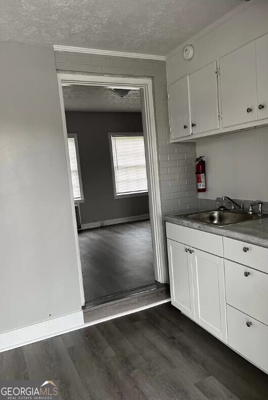 kitchen with a textured ceiling, dark wood-type flooring, white cabinets, and sink