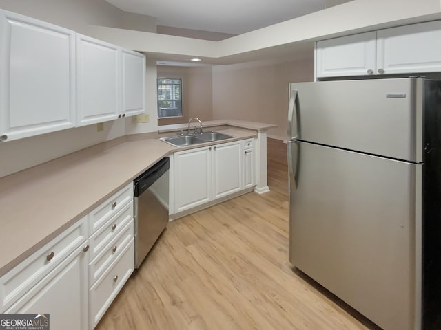 kitchen with sink, kitchen peninsula, appliances with stainless steel finishes, white cabinets, and light wood-type flooring