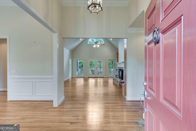 foyer featuring ornamental molding, light wood-type flooring, ceiling fan with notable chandelier, and a high ceiling