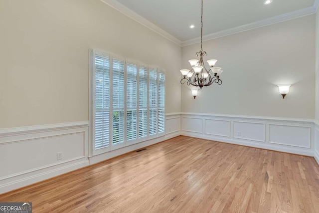 empty room with an inviting chandelier, crown molding, and light hardwood / wood-style flooring