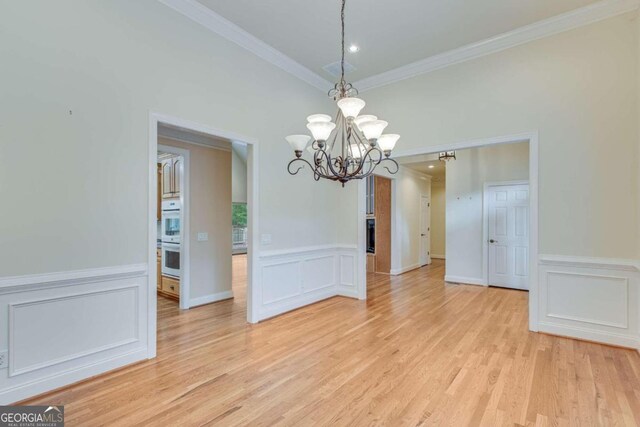 unfurnished dining area featuring an inviting chandelier, crown molding, and light hardwood / wood-style flooring