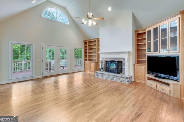 unfurnished living room with high vaulted ceiling, a brick fireplace, ceiling fan, and light wood-type flooring