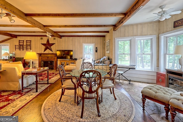 dining area with beam ceiling, wood-type flooring, wood walls, ceiling fan, and a healthy amount of sunlight