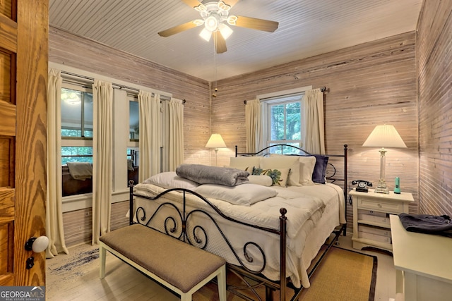 bedroom featuring light hardwood / wood-style floors, ceiling fan, and wooden walls