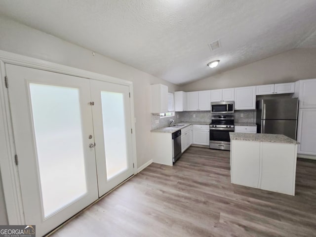 kitchen with light hardwood / wood-style floors, white cabinetry, vaulted ceiling, appliances with stainless steel finishes, and backsplash