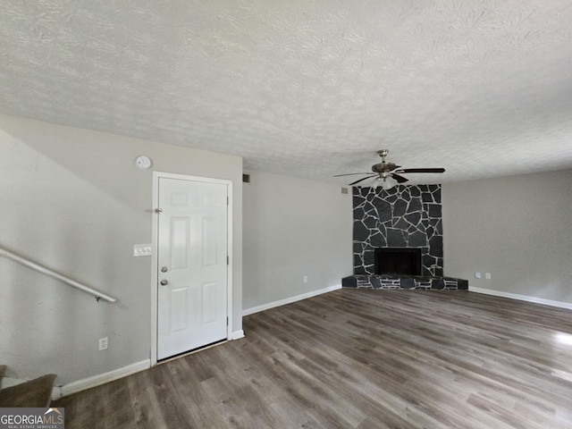 unfurnished living room featuring hardwood / wood-style flooring, ceiling fan, a stone fireplace, and a textured ceiling