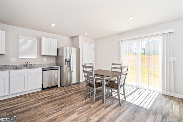 kitchen with light stone countertops, stainless steel appliances, hardwood / wood-style floors, white cabinets, and sink