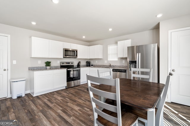 kitchen with light stone counters, dark hardwood / wood-style floors, white cabinetry, appliances with stainless steel finishes, and sink