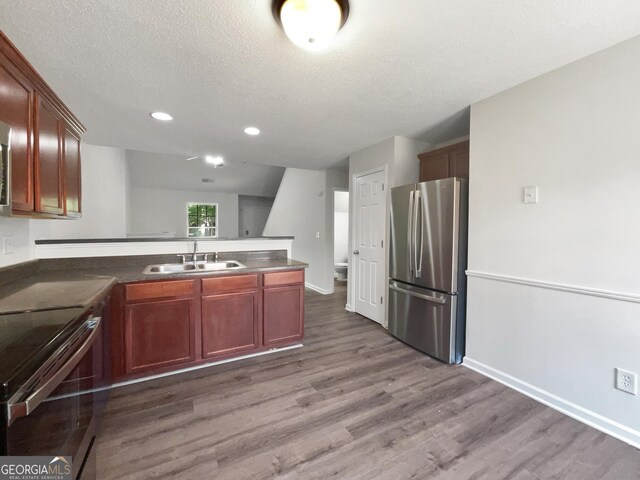 kitchen with sink, dark hardwood / wood-style flooring, kitchen peninsula, stainless steel appliances, and a textured ceiling