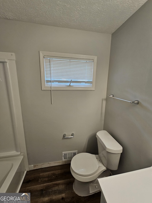 bathroom with hardwood / wood-style floors, a tub to relax in, vanity, toilet, and a textured ceiling