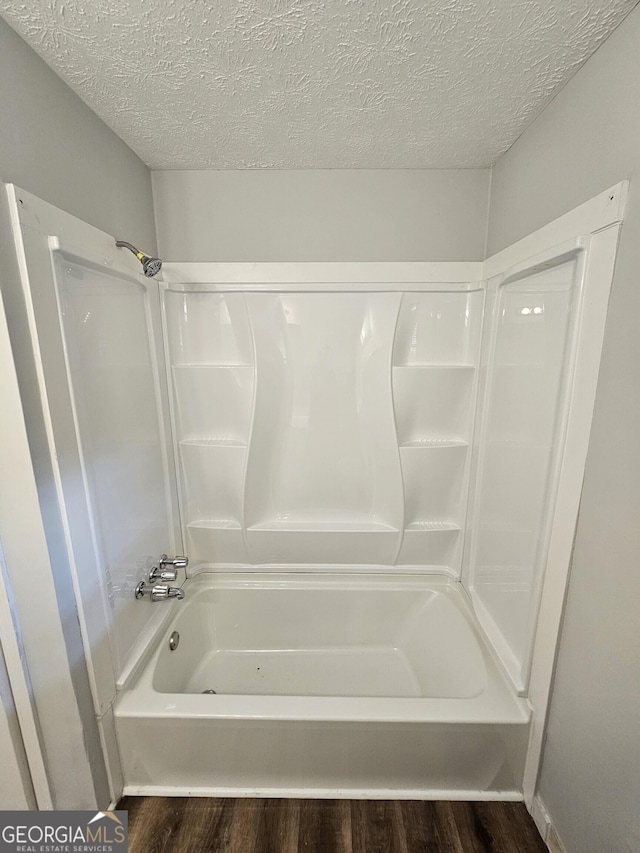 bathroom with wood-type flooring, tub / shower combination, and a textured ceiling