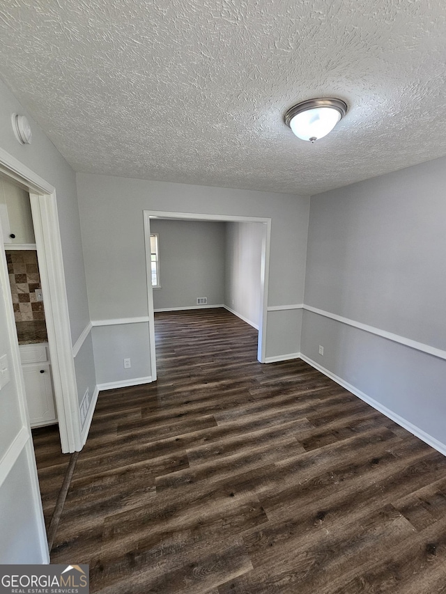 empty room with dark wood-type flooring and a textured ceiling