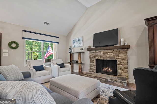 living room with a stone fireplace, wood-type flooring, and lofted ceiling