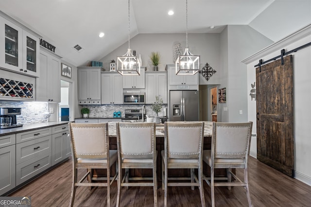 kitchen featuring stainless steel appliances, a barn door, backsplash, pendant lighting, and a kitchen island