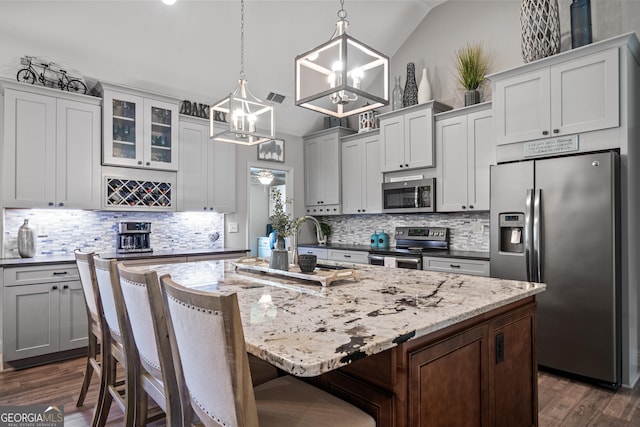 kitchen with appliances with stainless steel finishes, hanging light fixtures, lofted ceiling, and an island with sink