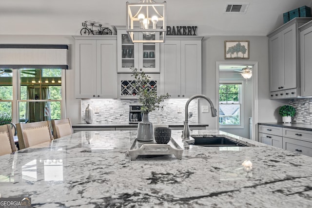 kitchen featuring tasteful backsplash, light stone counters, hanging light fixtures, and sink