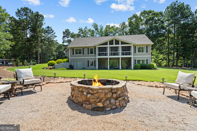 rear view of property featuring a lawn, a patio area, a sunroom, and an outdoor fire pit