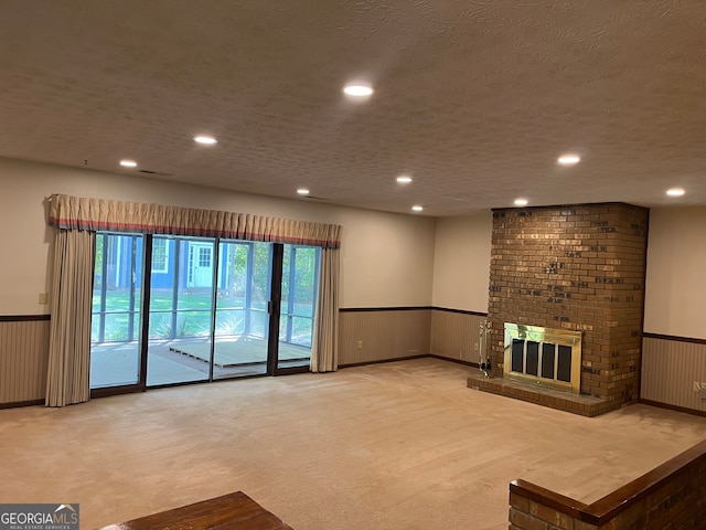 unfurnished living room with a brick fireplace, a textured ceiling, wood walls, and carpet