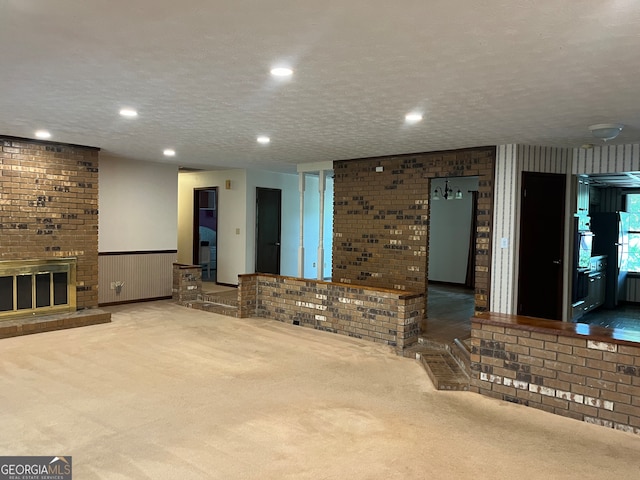 unfurnished living room with a brick fireplace, light colored carpet, and a textured ceiling