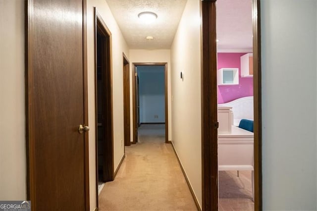 hallway with light carpet and a textured ceiling