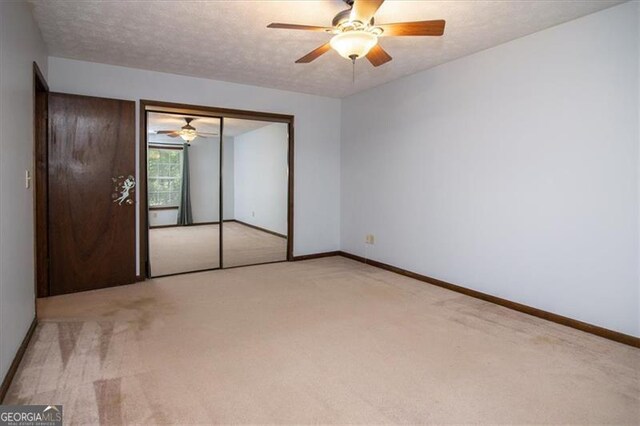 unfurnished bedroom featuring a textured ceiling, ceiling fan, light carpet, and a closet