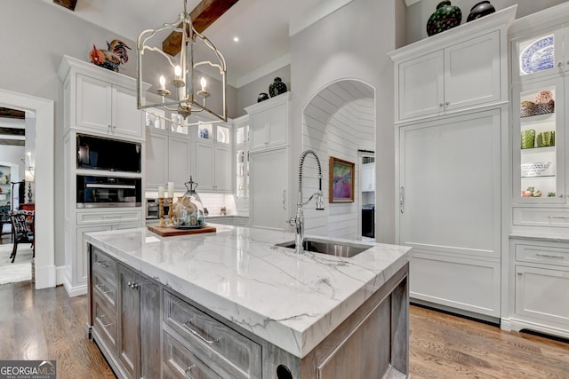 962 Chattooga Trce, Suwanee, GA 30024 - kitchen with a chandelier, an island with sink, white cabinets, wood finished floors, and glass insert cabinets