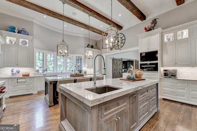 962 Chattooga Trce, Suwanee, GA 30024 - kitchen with a kitchen island with sink, a chandelier, tasteful backsplash, white cabinetry, and beamed ceiling