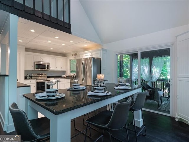 kitchen featuring appliances with stainless steel finishes, white cabinetry, dark wood-type flooring, high vaulted ceiling, and a breakfast bar area