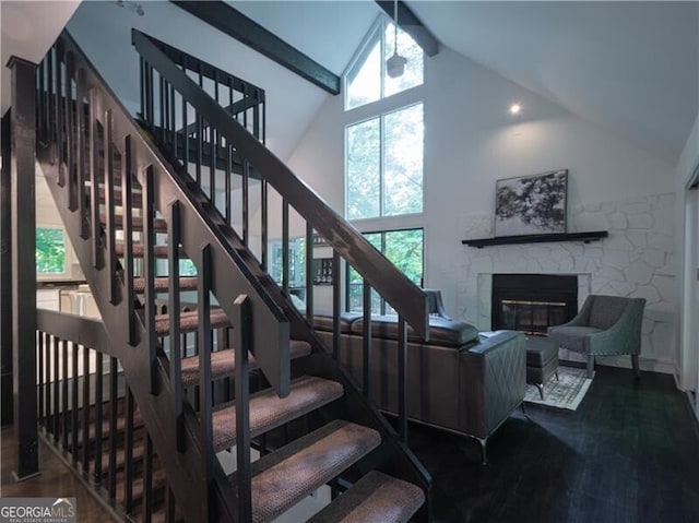 stairs featuring high vaulted ceiling, a stone fireplace, and beam ceiling